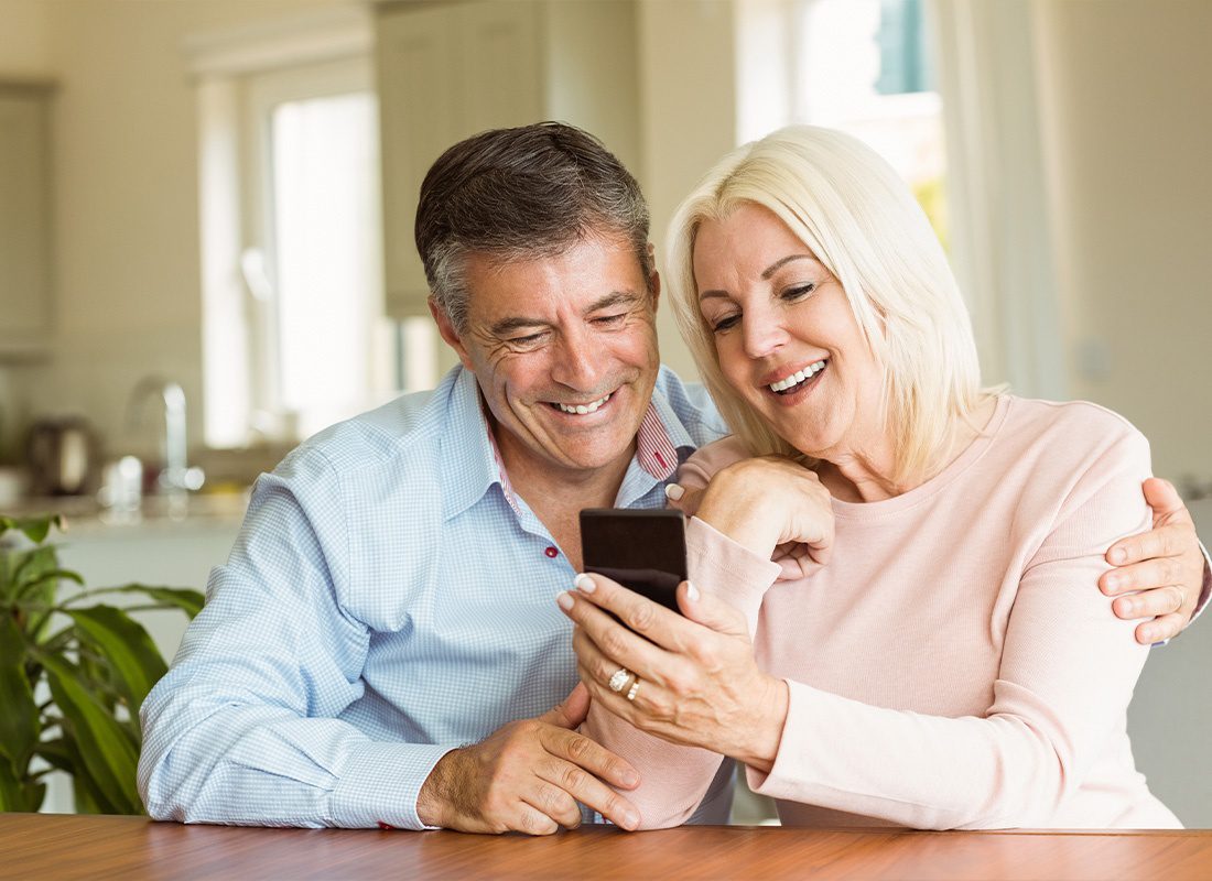 Read Our Reviews - Happy Middle Aged Couple Looking at a Smartphone Together at Home